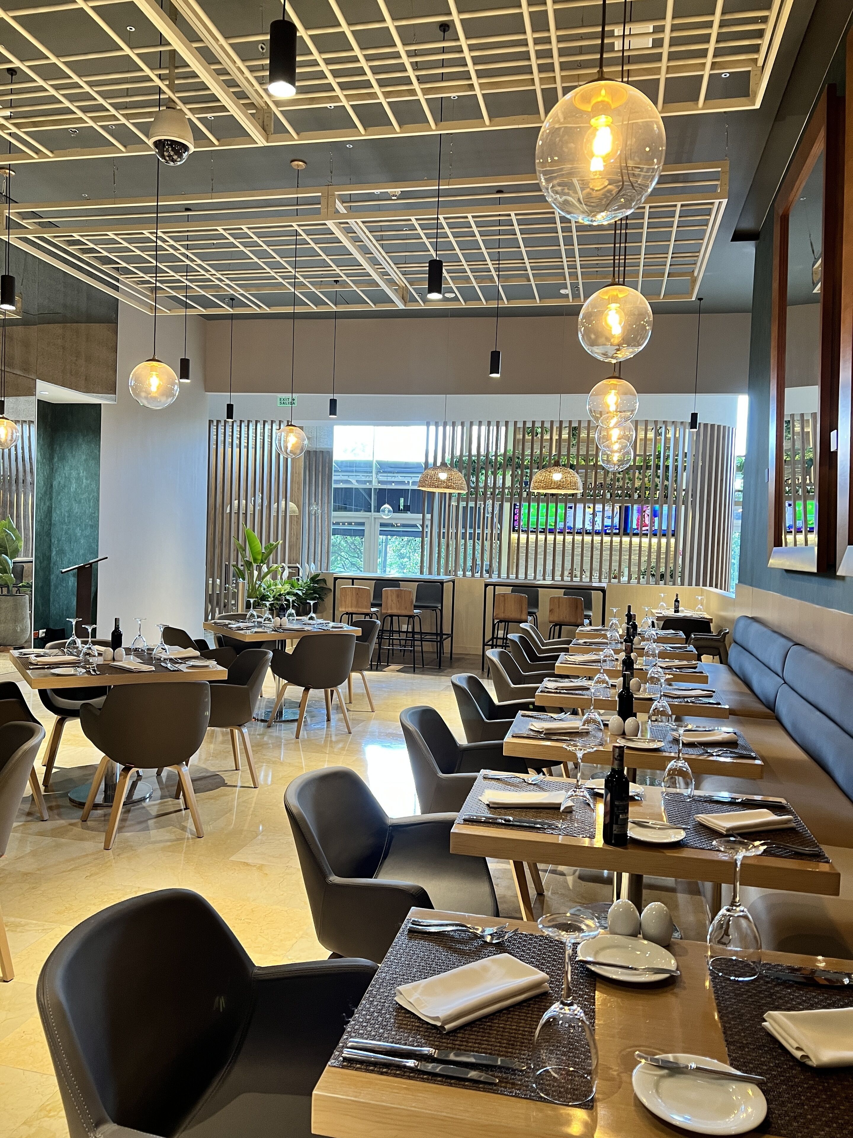 A modern dining area with long tables, black chairs, and hanging spherical light fixtures.