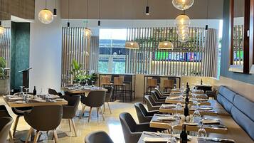 A modern dining area with long tables, black chairs, and hanging spherical light fixtures.