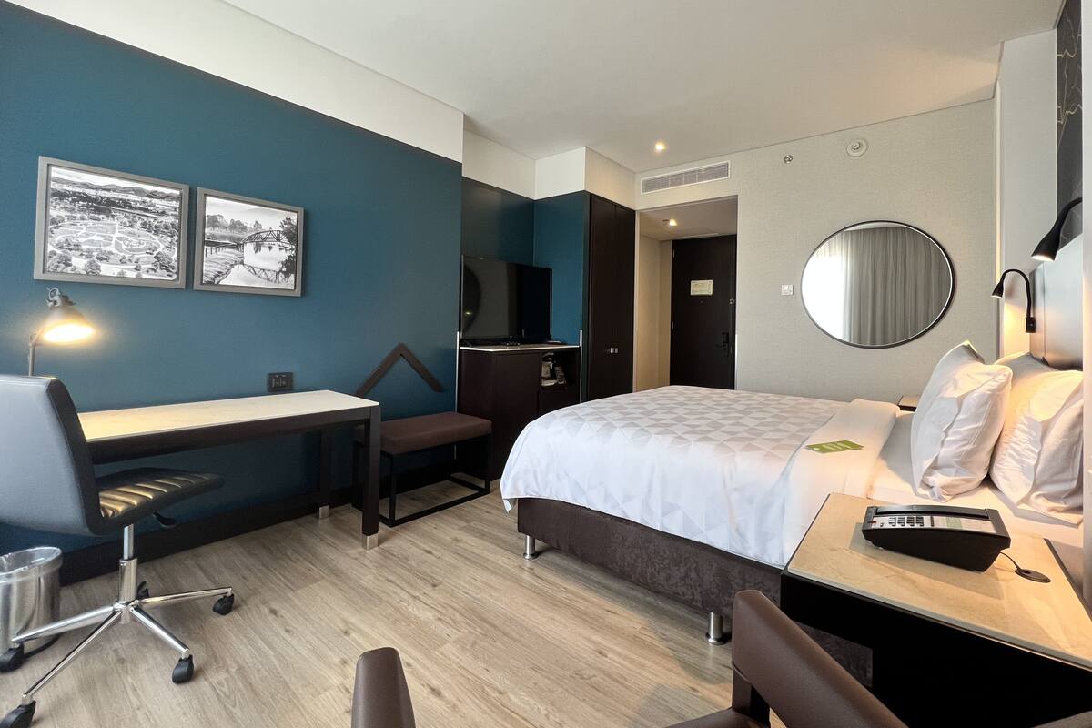 A hotel room with a bed, desk, chair, and a TV.