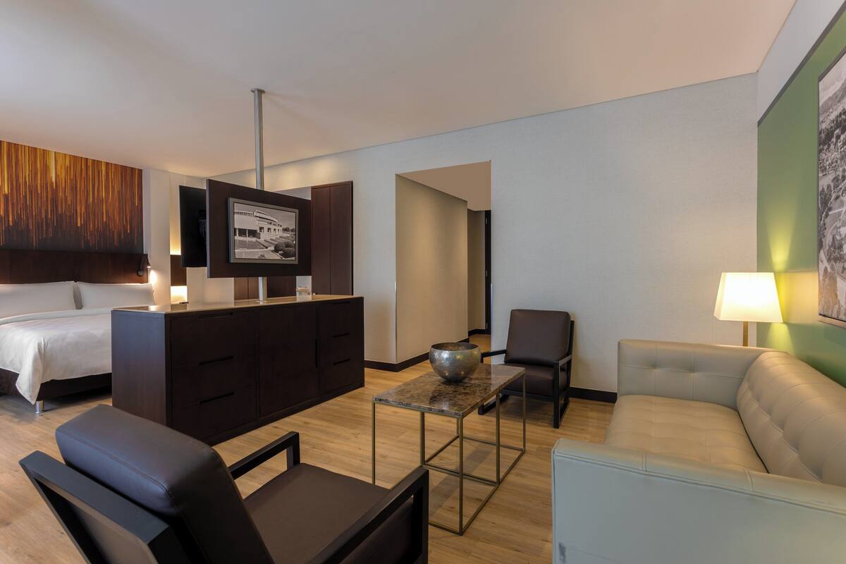 A modern hotel room with a bed, a sofa, a coffee table, a TV, and a desk.