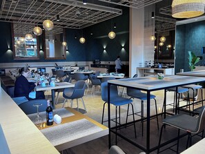A modern restaurant interior with high ceilings, pendant lighting, and a mix of seating arrangements including tables and chairs.