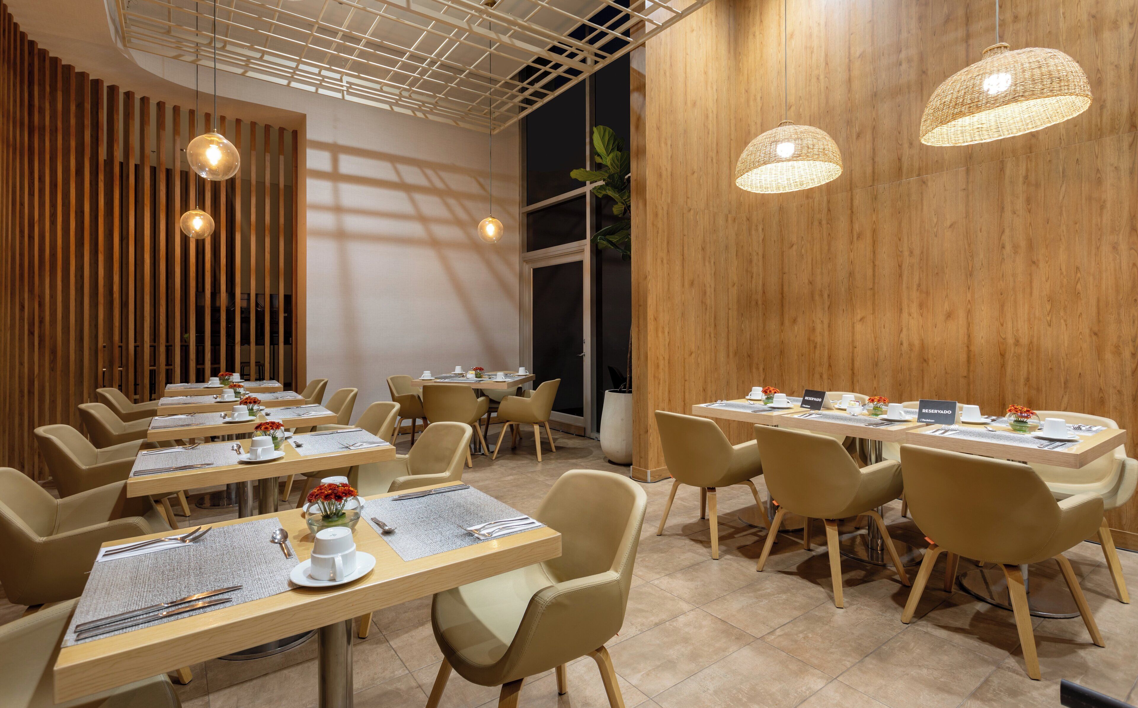A modern dining area with wooden panel walls, multiple tables with chairs, and hanging pendant lights.