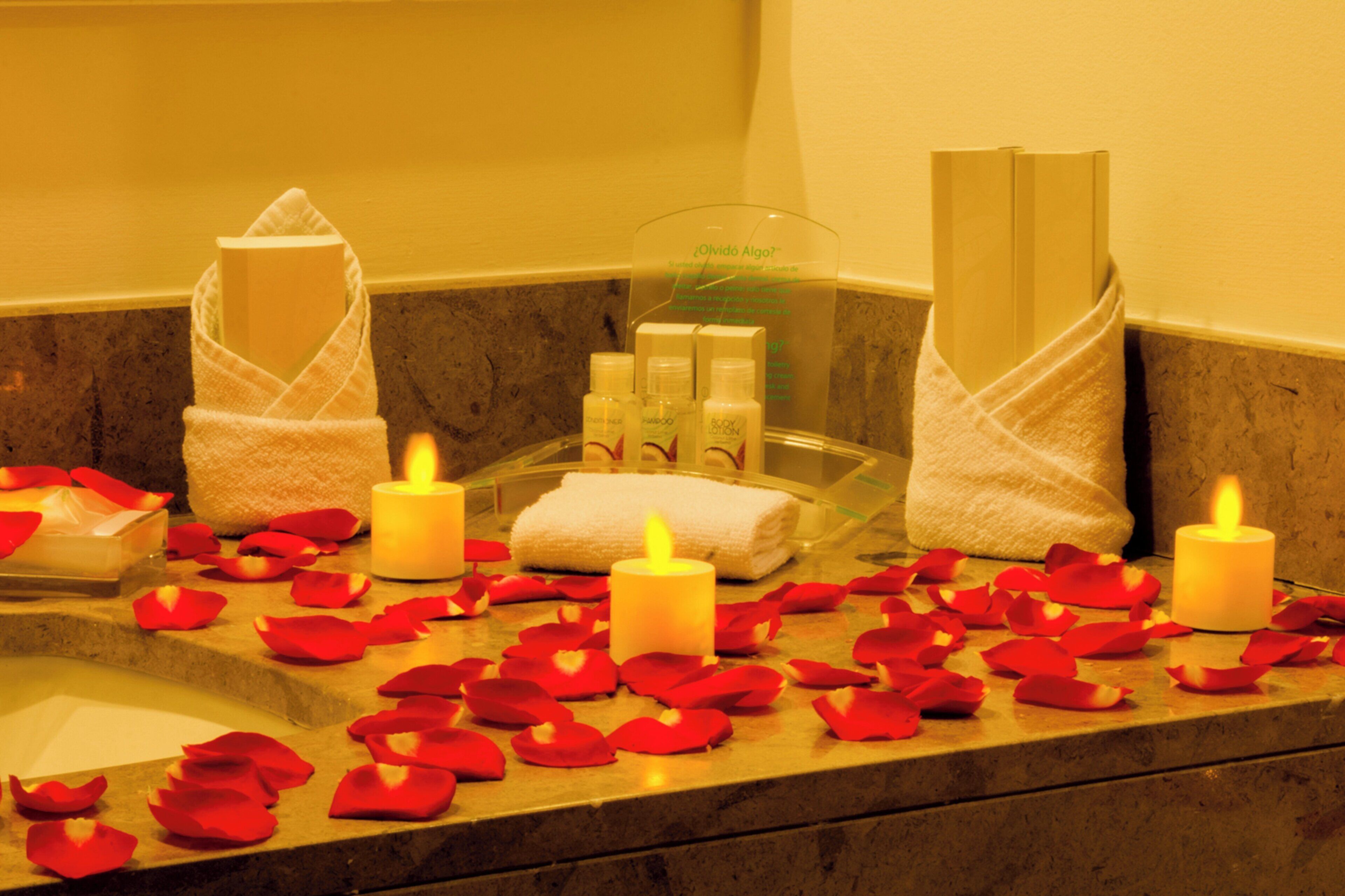 A bathroom with a bathtub, candles, rose petals, and toiletries.
