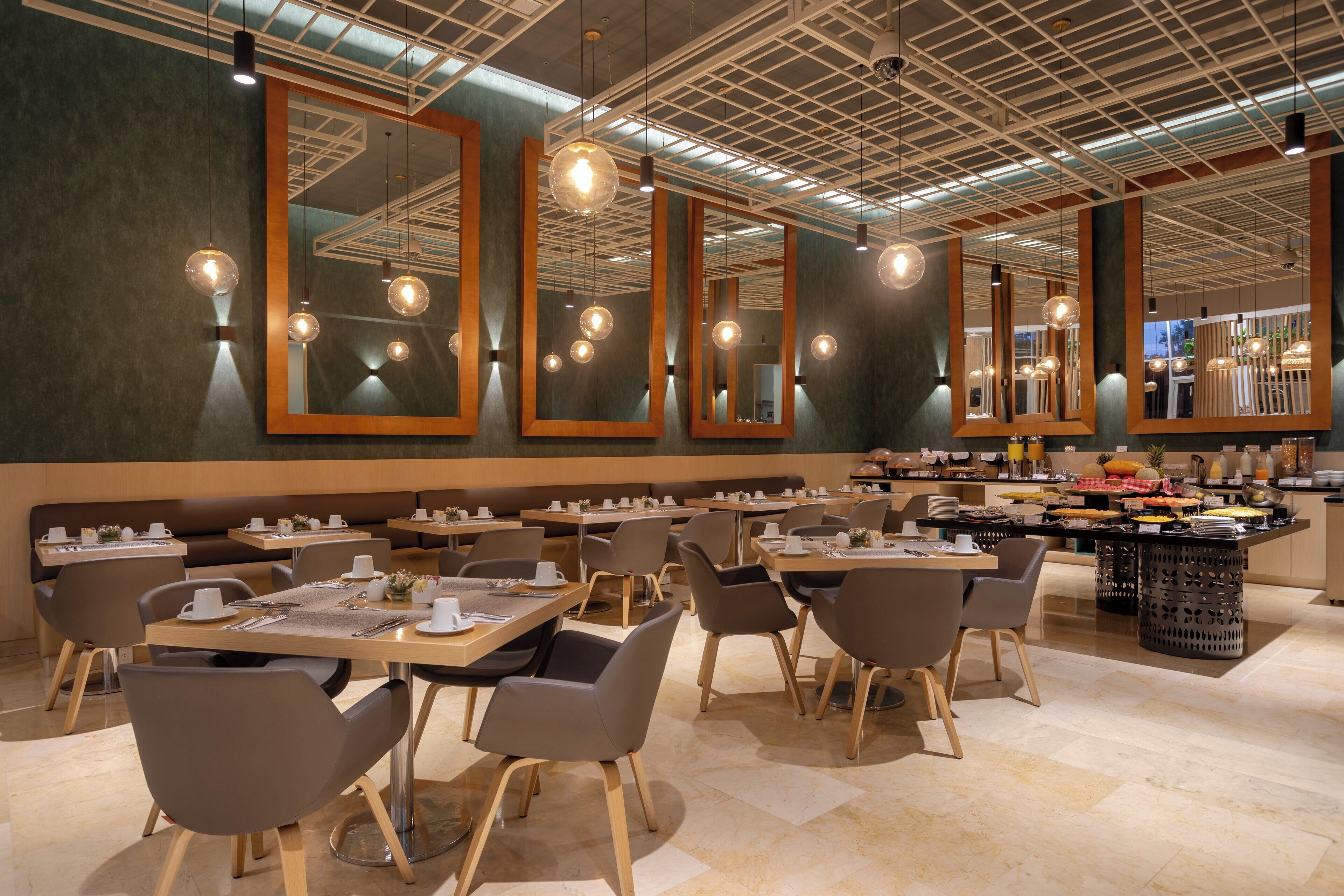 Un ristorante moderno con diversi tavoli e sedie, ampi specchi alle pareti e lampade a sospensione.