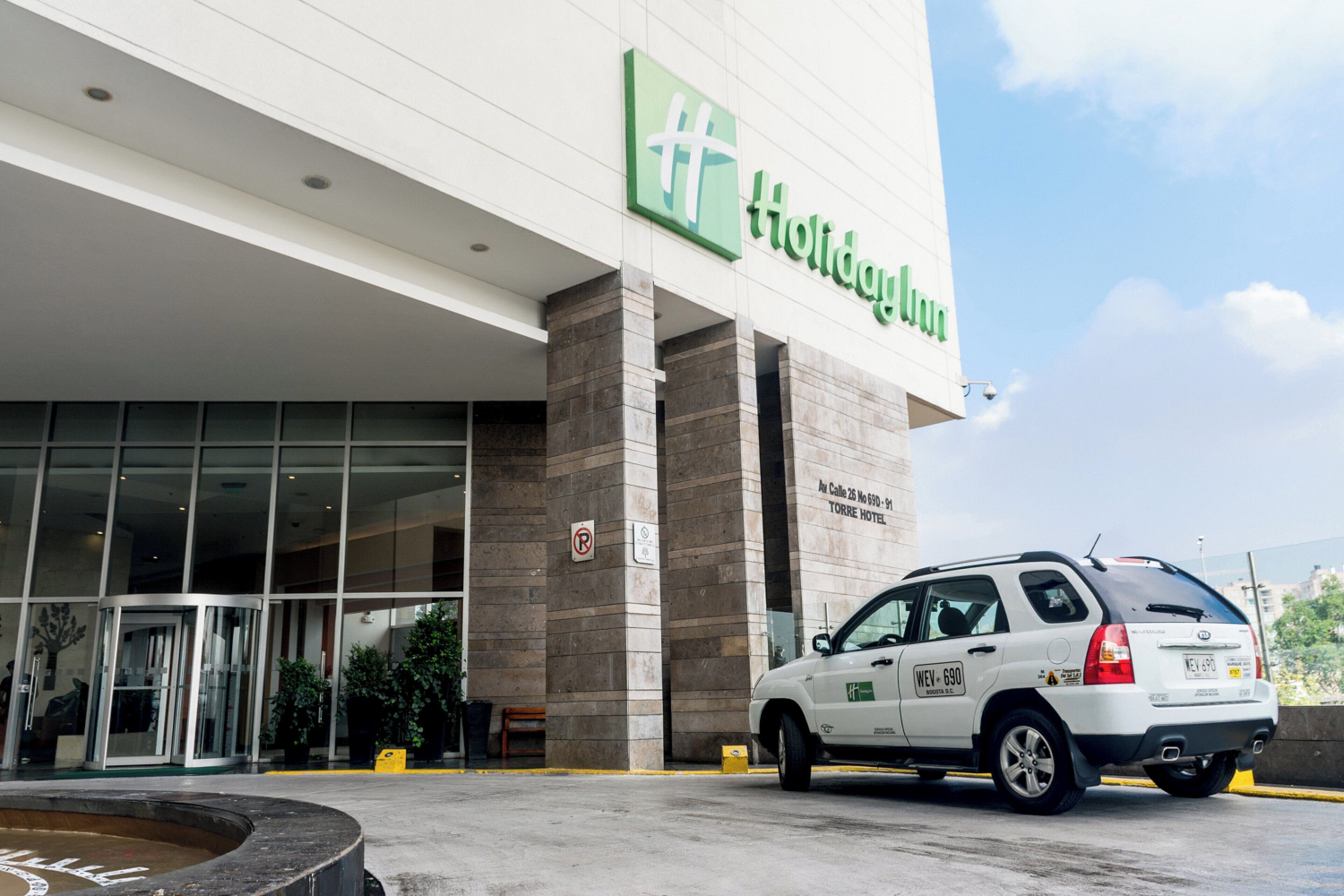 L’entrée d’un hôtel, avec une enseigne « Holiday Inn », une voiture garée devant et un panneau « stationnement interdit » sur le mur.