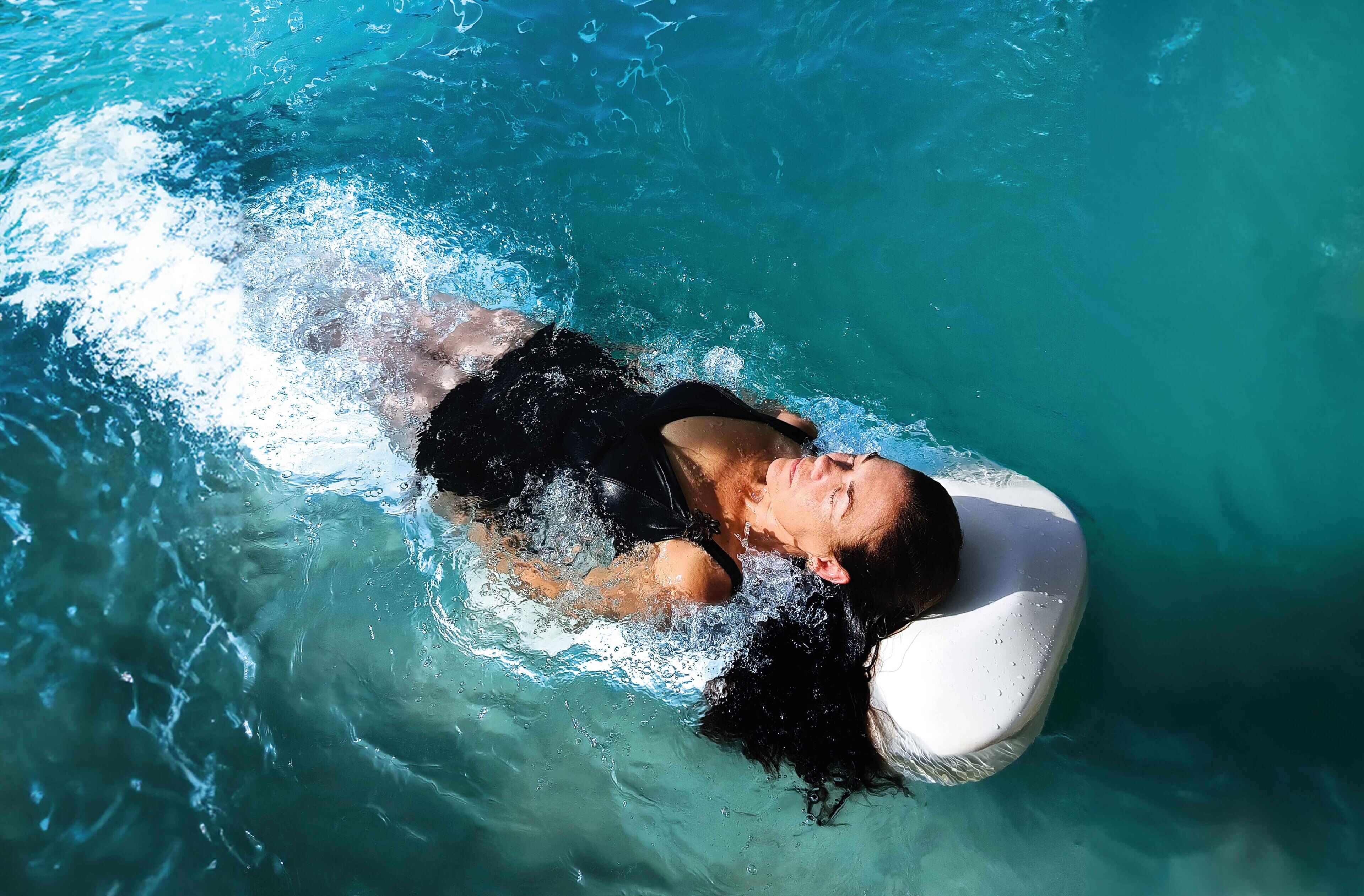 A person floating in a pool with a clear blue water surface.