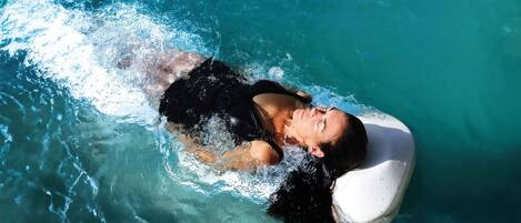 A person floating in a pool with a clear blue water surface.
