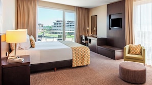 A hotel room with a large bed, a desk, a TV, and a view of buildings.