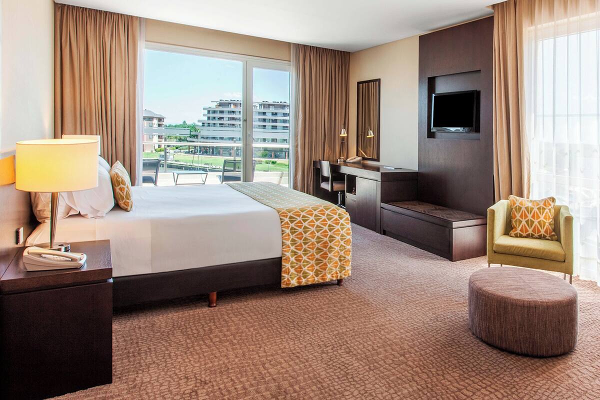 Habitación de hotel con una cama grande, un escritorio, un televisor y vistas a edificios.
