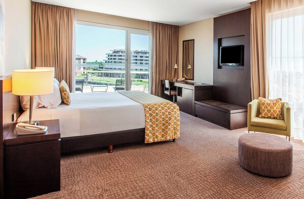 A hotel room with a large bed, a desk, a TV, and a view of buildings. - Wyndham Nordelta Tigre Buenos Aires (Nordelta)