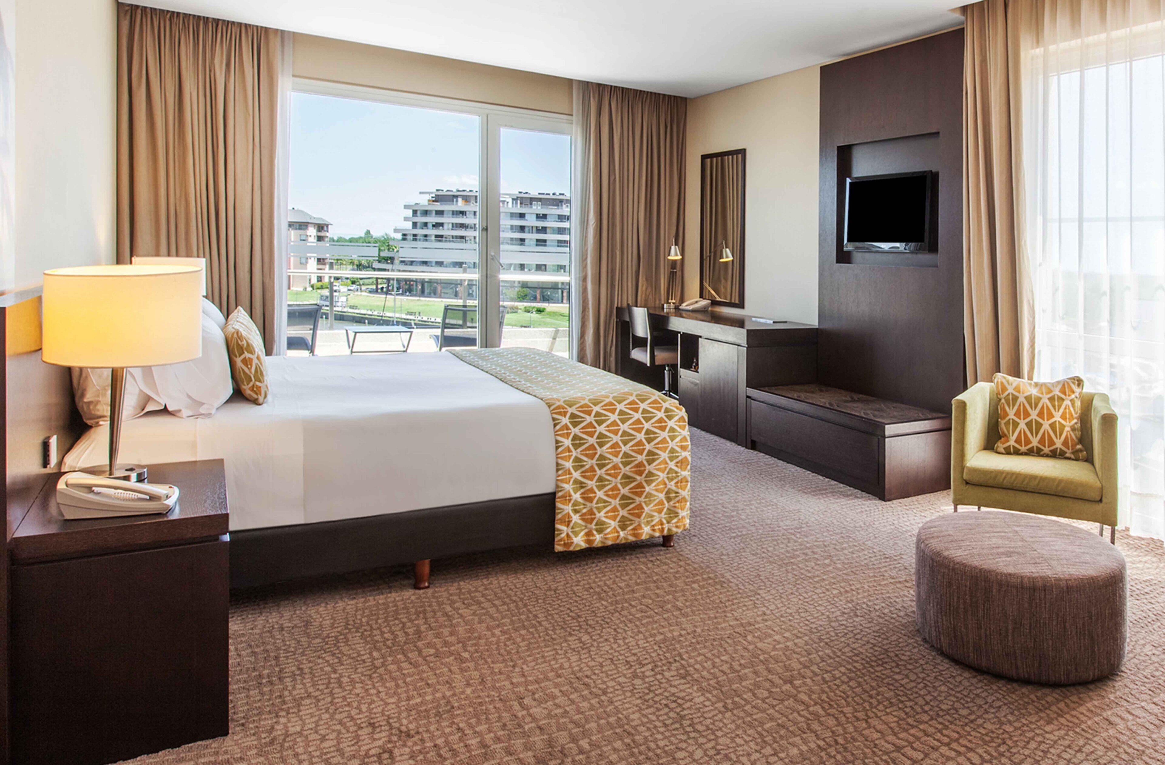 Quarto de hotel com uma cama grande, uma escrivaninha, uma cadeira, uma televisão e vista para edifícios.