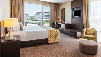 Quarto de hotel com uma cama grande, uma escrivaninha, uma cadeira, uma televisão e vista para edifícios.