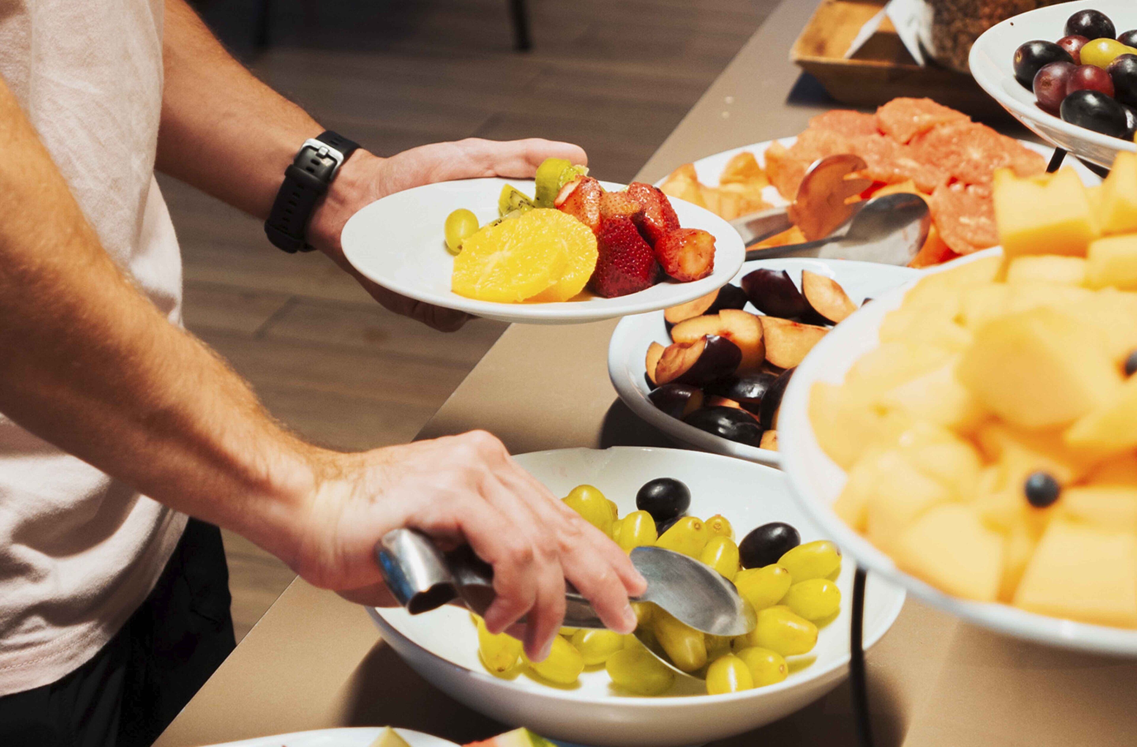 Una persona servándose comida de un bufé con diversas frutas y verduras.