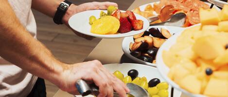Una persona servándose comida de un bufé con diversas frutas y verduras.