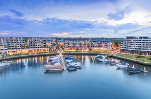 A marina with multiple boats docked, surrounded by multi-story buildings with balconies.