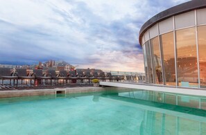 Piscina en la azotea con sillones de descanso y balaustrada de vidrio con vista a un paisaje urbano.