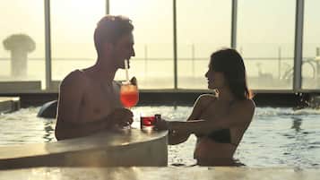 A couple in a heated pool with a drink, large windows, and a view of the water.