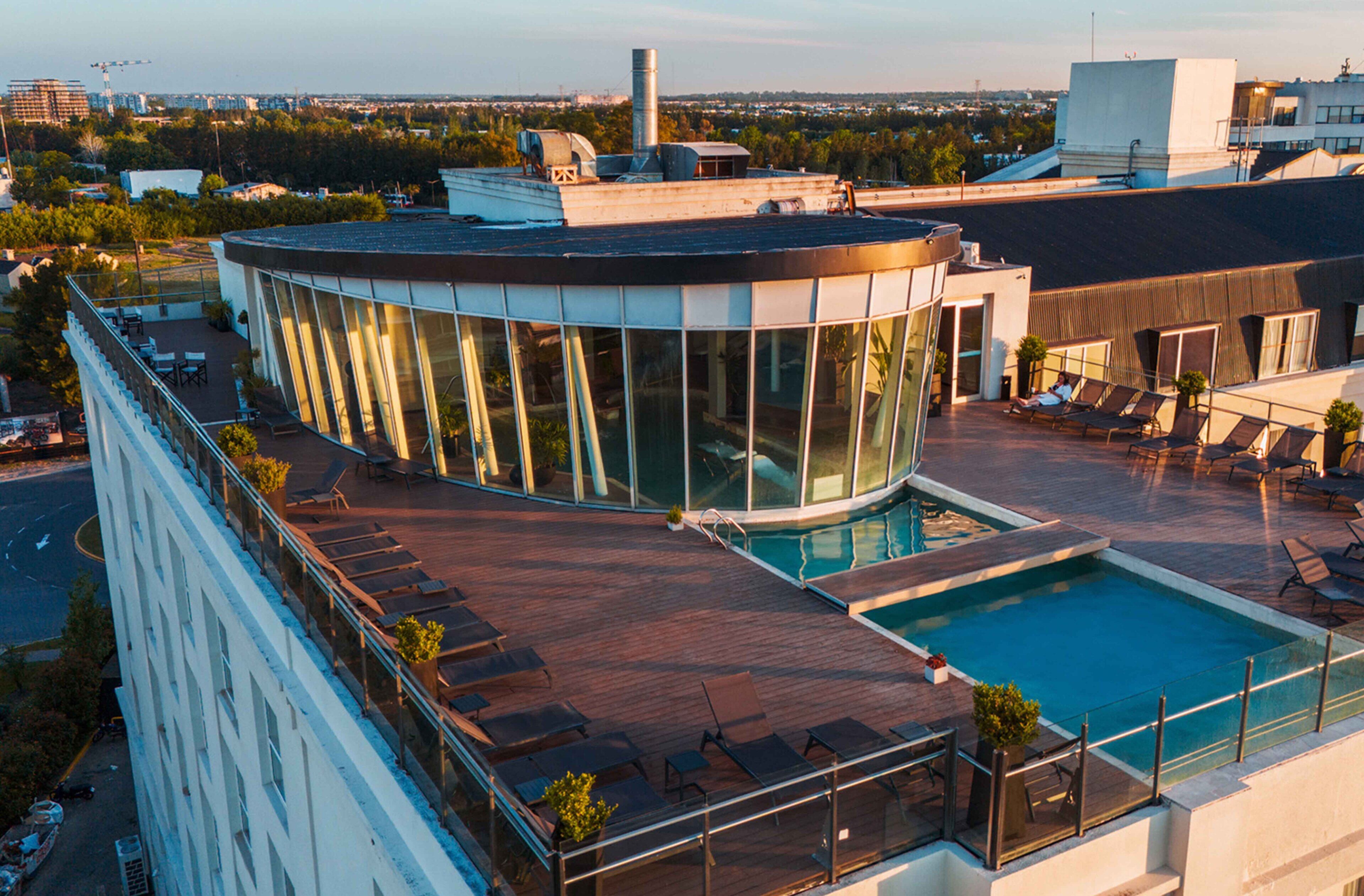 Un edificio moderno con piscina en la azotea, paredes de vidrio y un área de descanso circular.