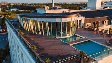 Un edificio moderno con piscina en la azotea, paredes de vidrio y un área de descanso circular.