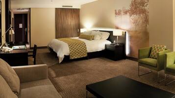 A hotel room with a bed, bedside tables, a desk, a green armchair, and a coffee table.