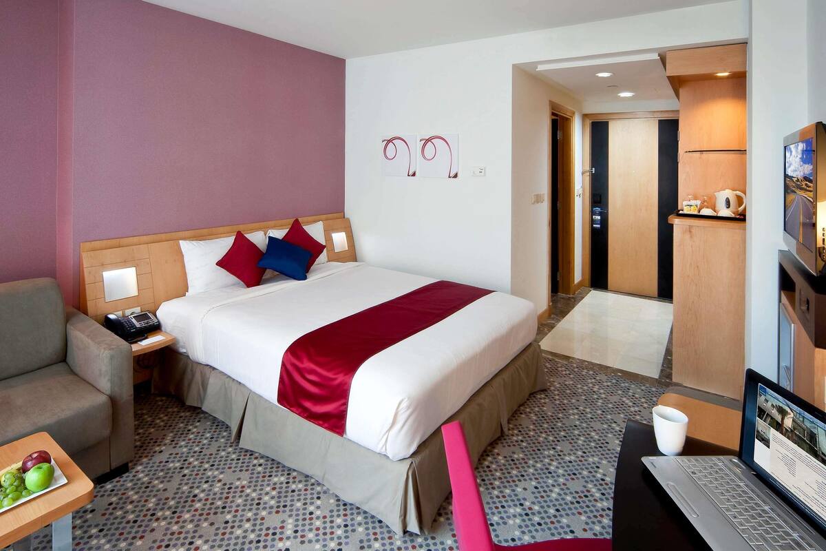 A hotel room with a bed, bedside tables, a desk, a chair, a laptop, and a TV.