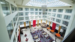 A multi-level hotel atrium with a central open space, multiple seating areas, and a large chandelier.