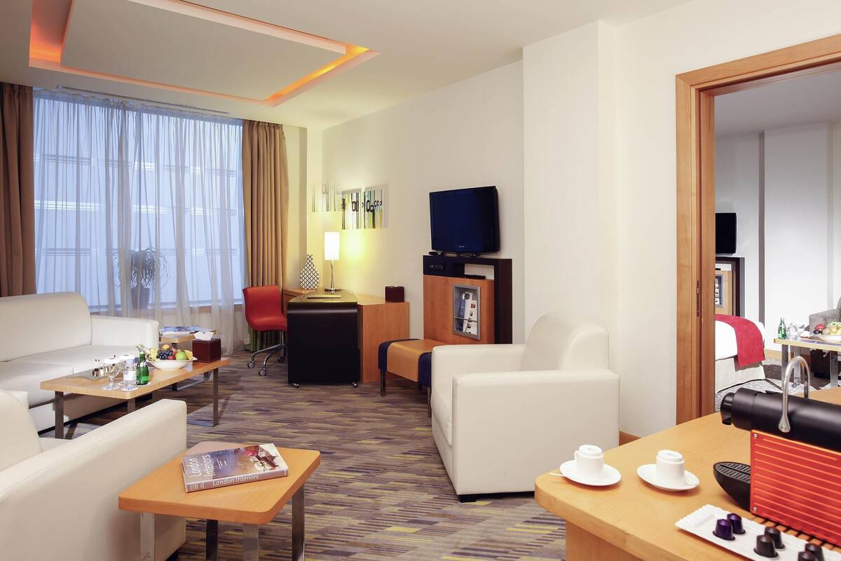 A hotel room with a sofa, a dining table, a TV, and a desk.
