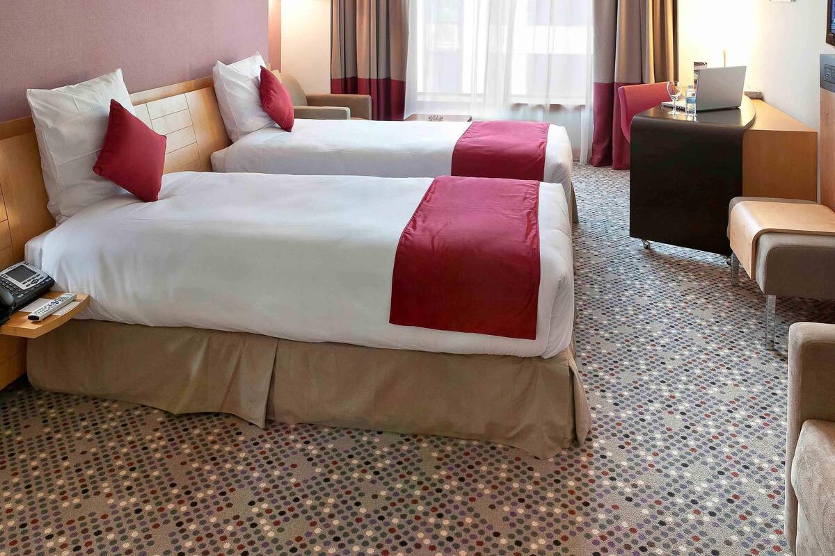 A hotel room with two beds, a desk, a chair, and a laptop.