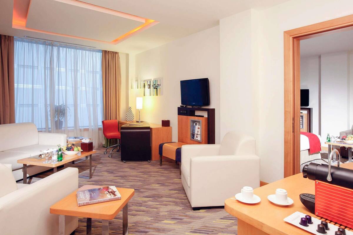 A hotel room with a sofa, a desk, a chair, a TV, and a coffee table.
