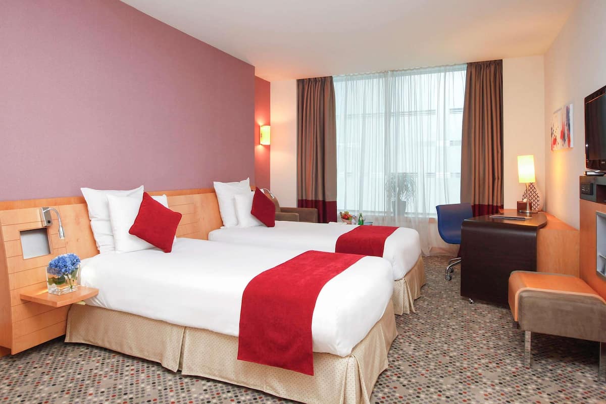A hotel room with two beds, a desk, a chair, a TV, and a window with curtains.
