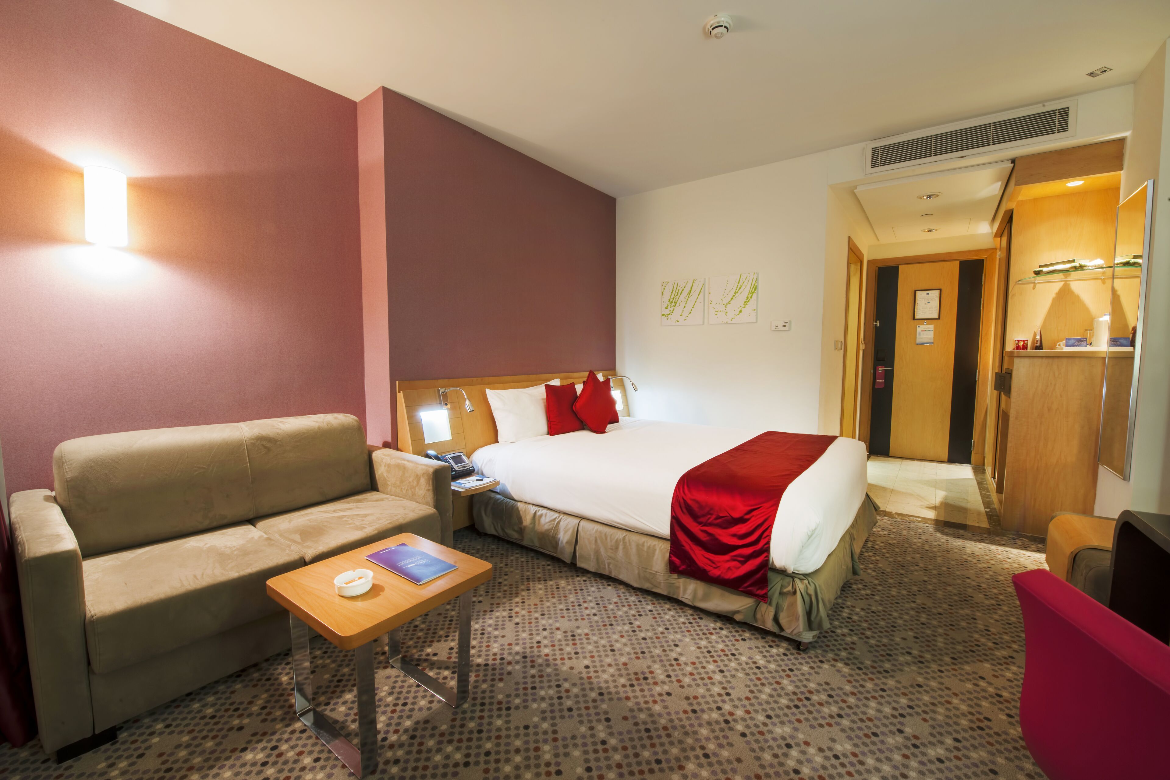 A hotel room with a bed, a sofa, a small table, and a mirror.