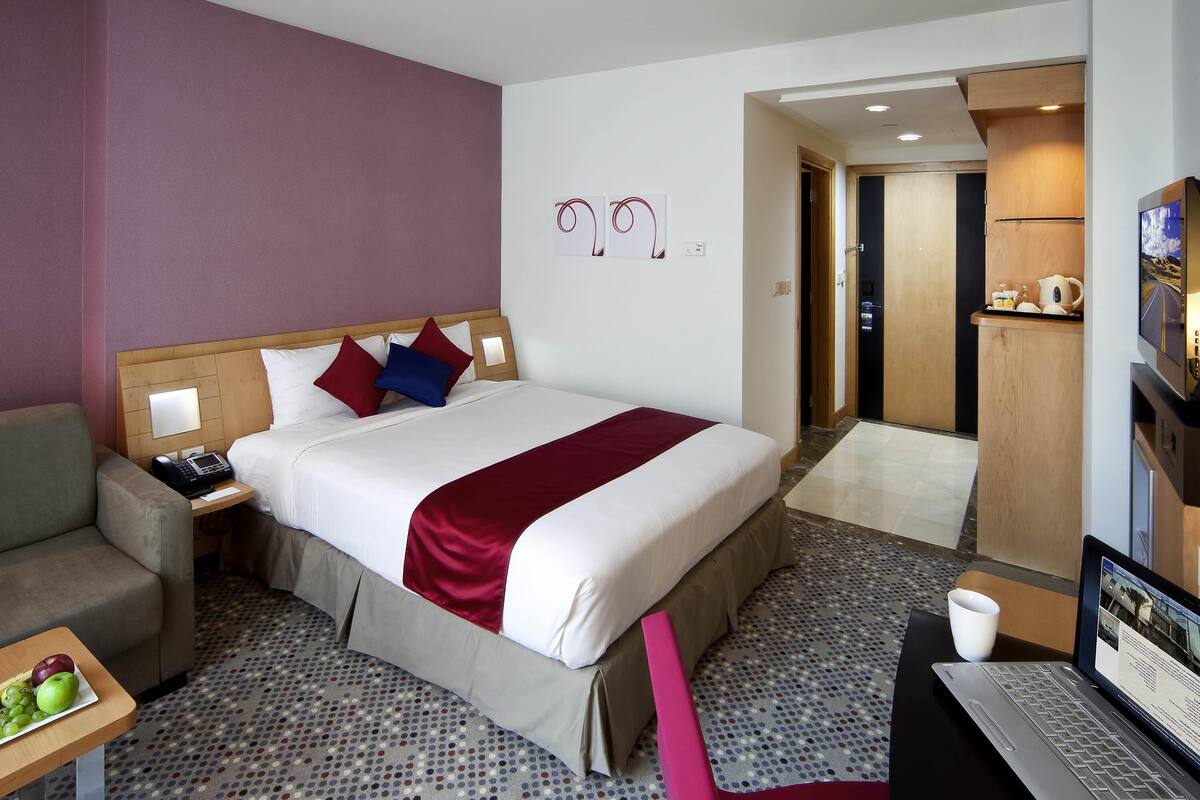 A hotel room with a bed, bedside table, lamp, and a desk with a laptop.