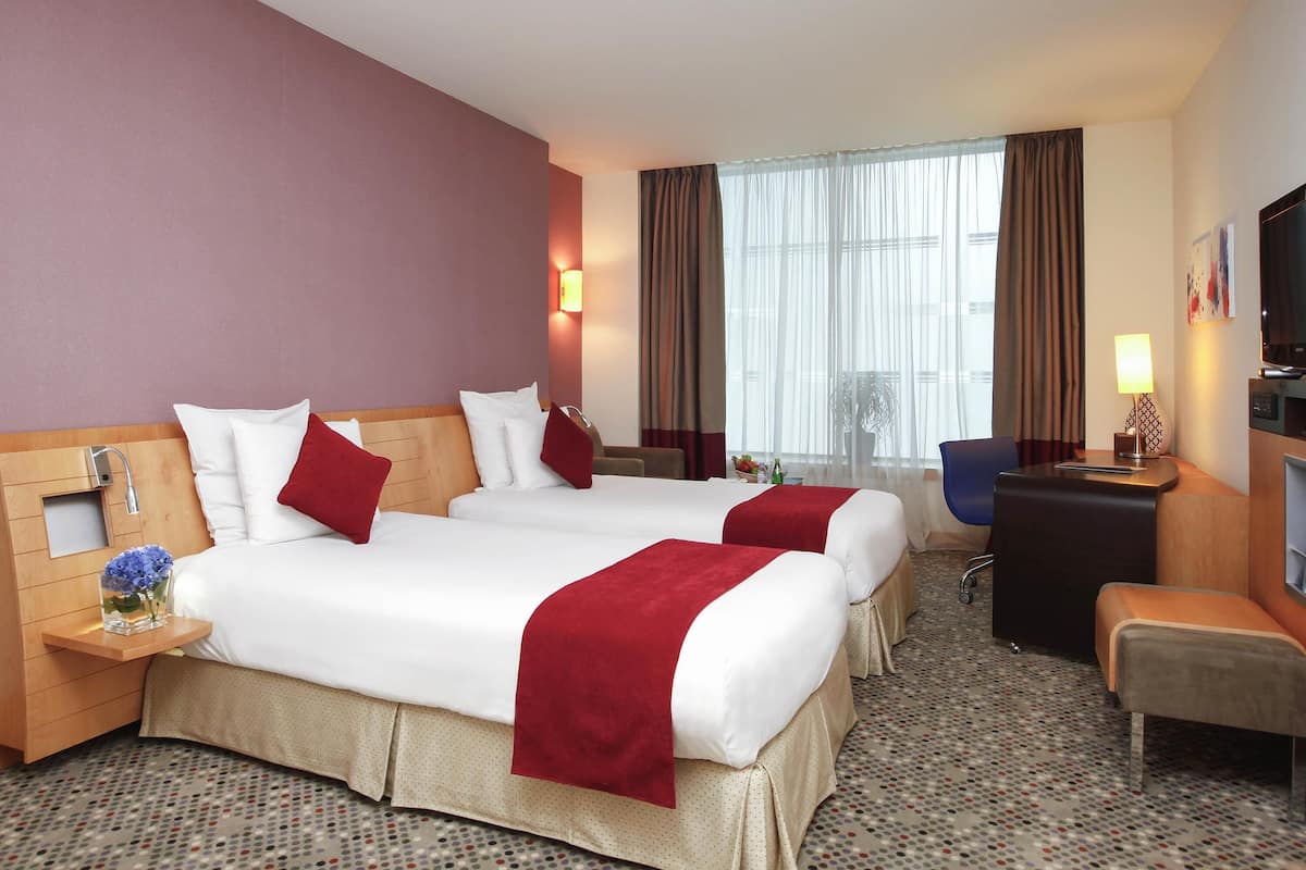Une chambre d’hôtel avec deux lits, un bureau, une chaise, une télévision et une fenêtre avec des rideaux.