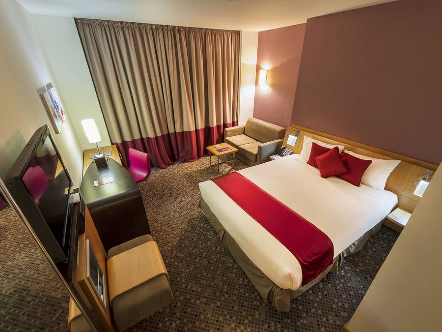 A hotel room with a large bed, a desk with a chair, a small table, and a TV.