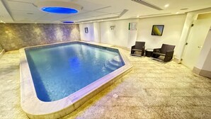 A swimming pool with a tiled deck, surrounded by a few chairs and a small table.