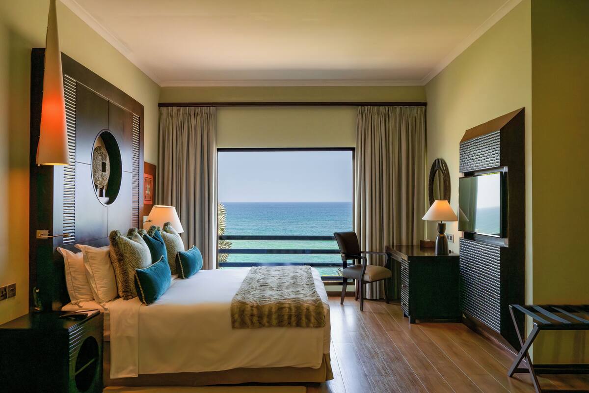 Une chambre d’hôtel avec un lit, un bureau, une chaise, une télévision et une vue sur l’océan.
