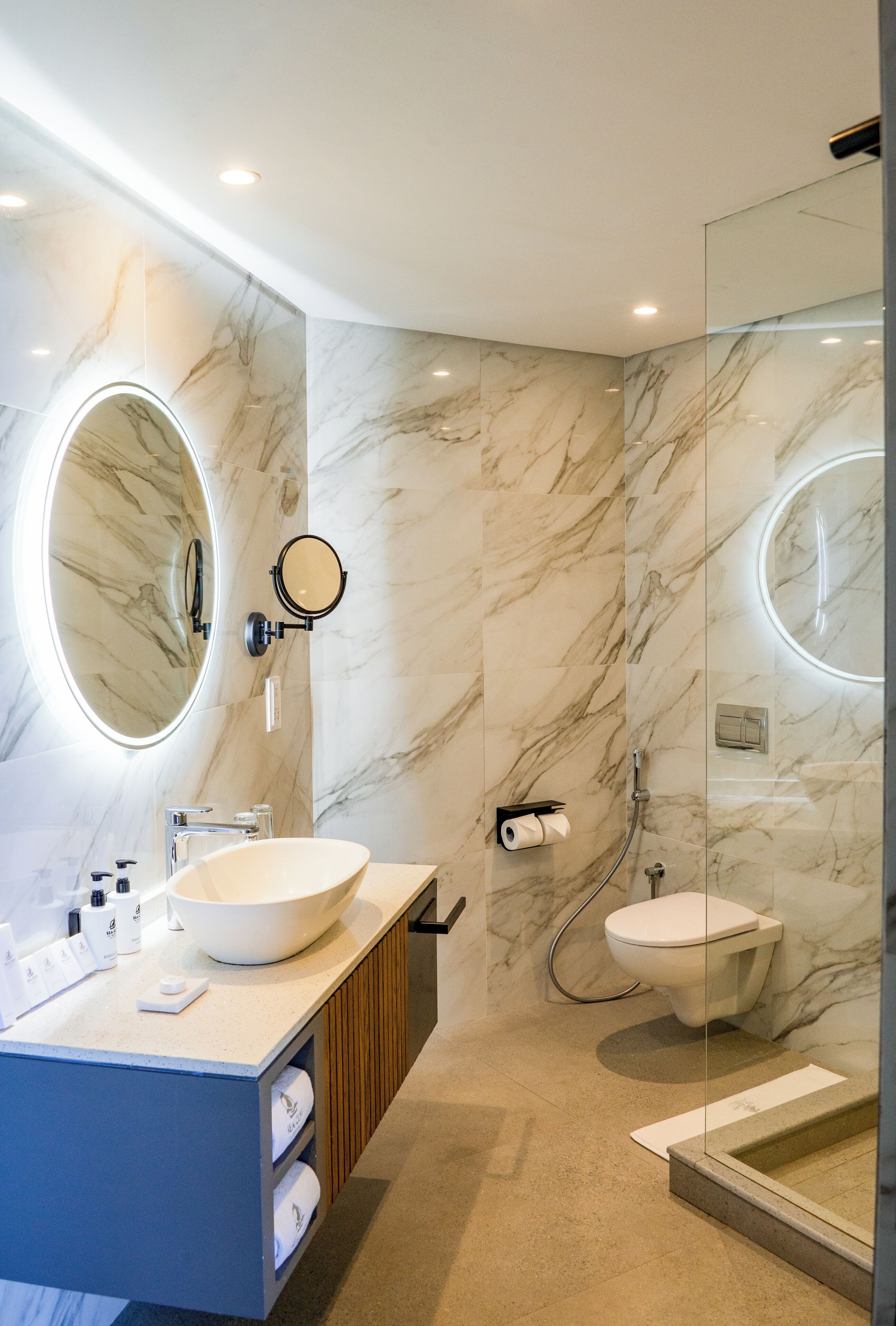 A modern bathroom with a marble wall, a round mirror, a sink, and a toilet.