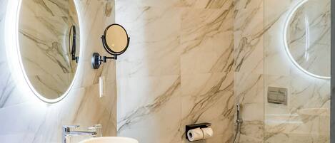 A modern bathroom with a marble wall, a round mirror, a sink, and a toilet.