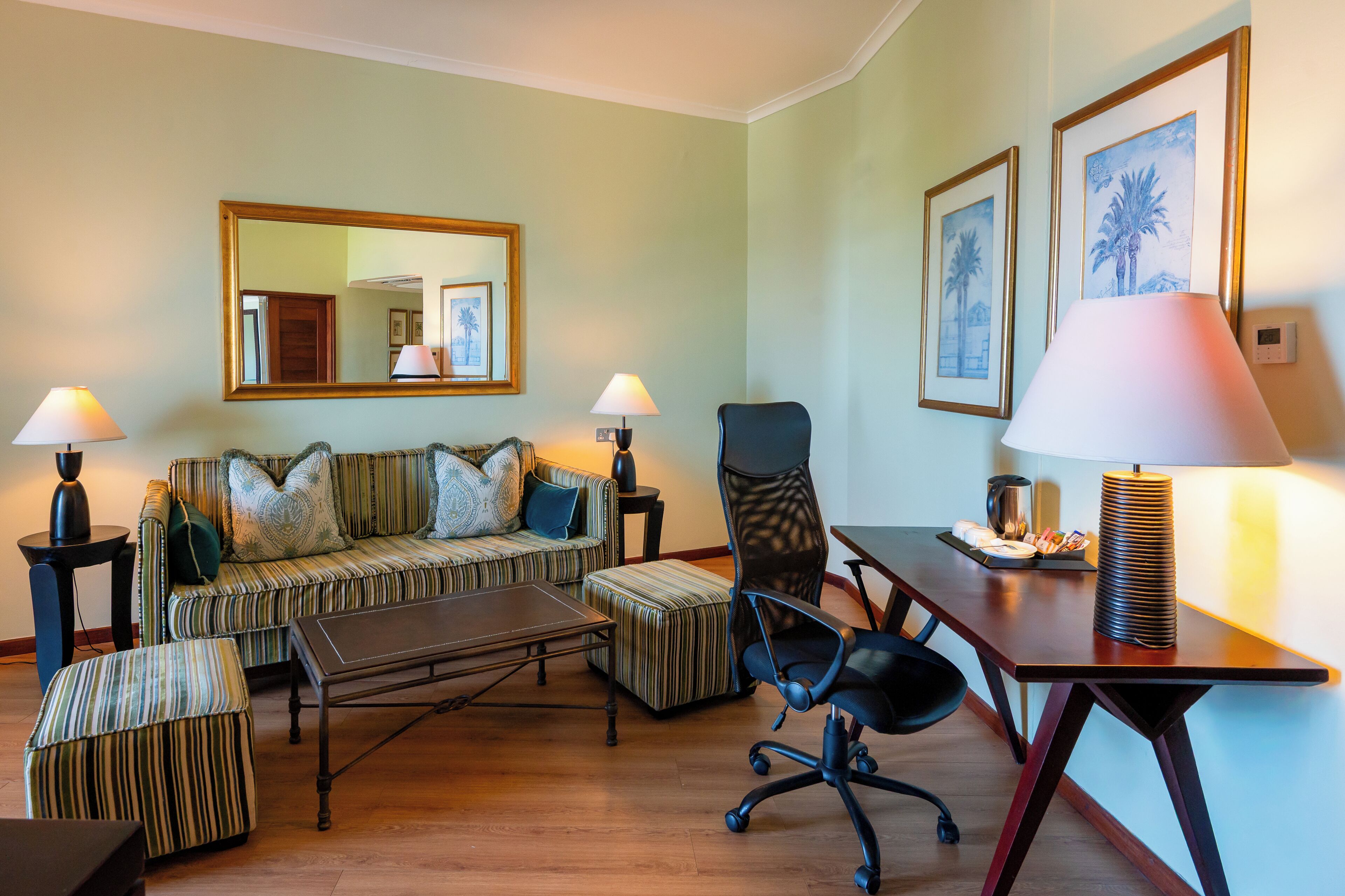 Un salon comprenant un canapé, un pouf, une table basse, un fauteuil de bureau, un bureau, des lampes et des œuvres d’art encadrées accrochées aux murs.