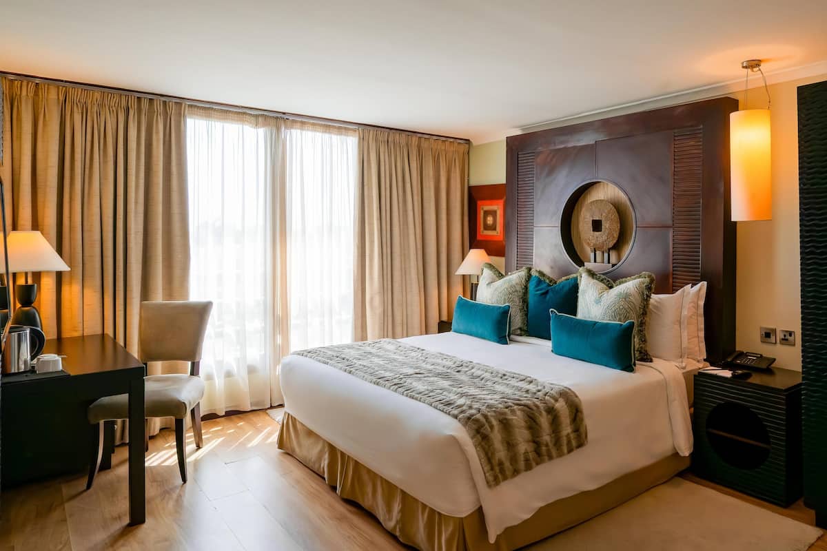 Une chambre d’hôtel avec un grand lit, un bureau, une chaise, une lampe et un haut-parleur fixé au mur.
