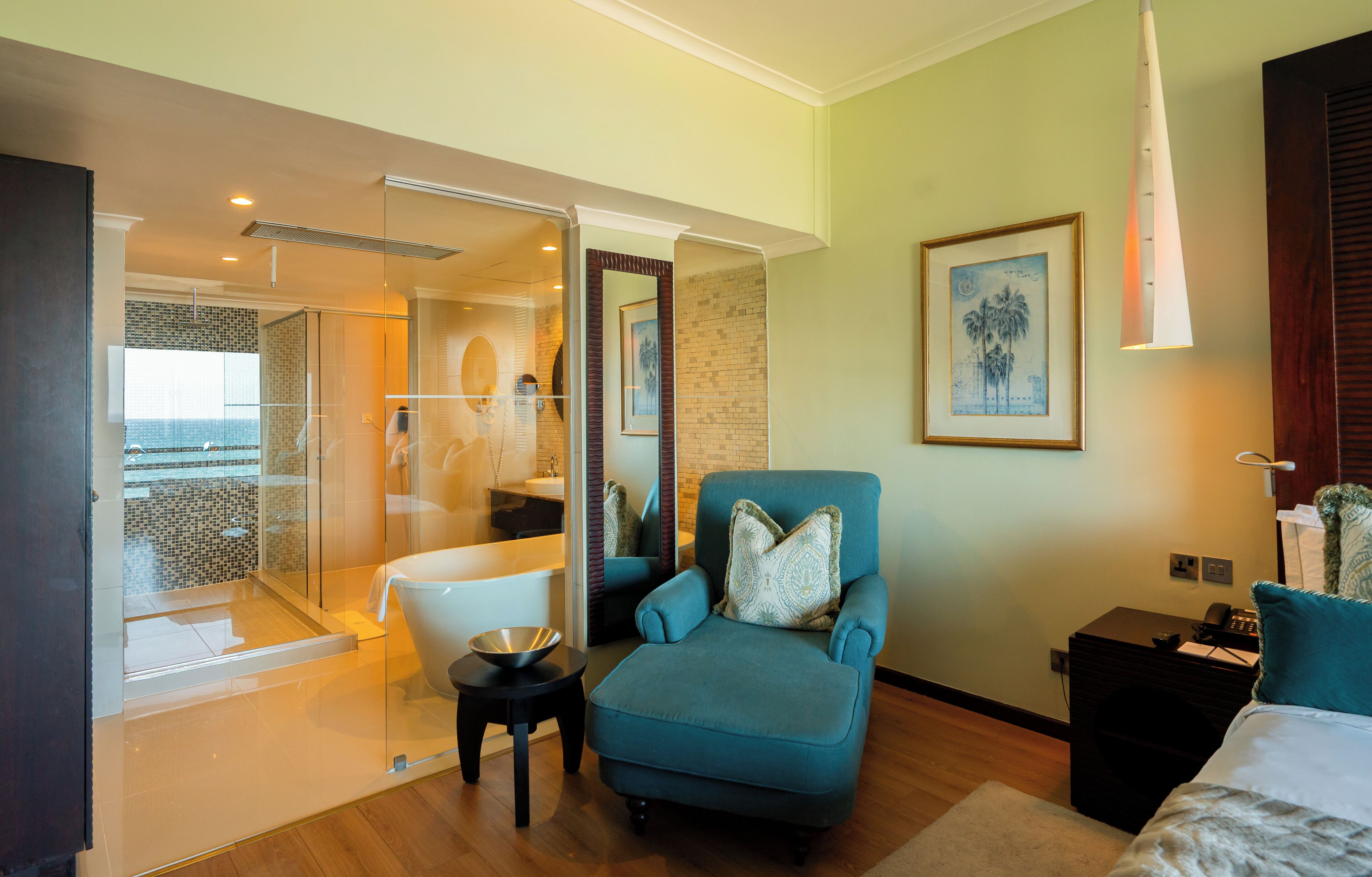 A modern hotel room with a balcony, a bathtub, a seating area with a chair and a small table, and a bed.