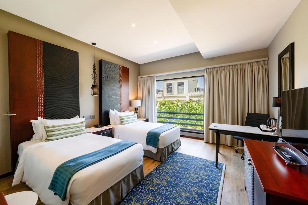 Une chambre d’hôtel avec deux lits, un bureau, une chaise, une télévision et un balcon avec des rideaux.