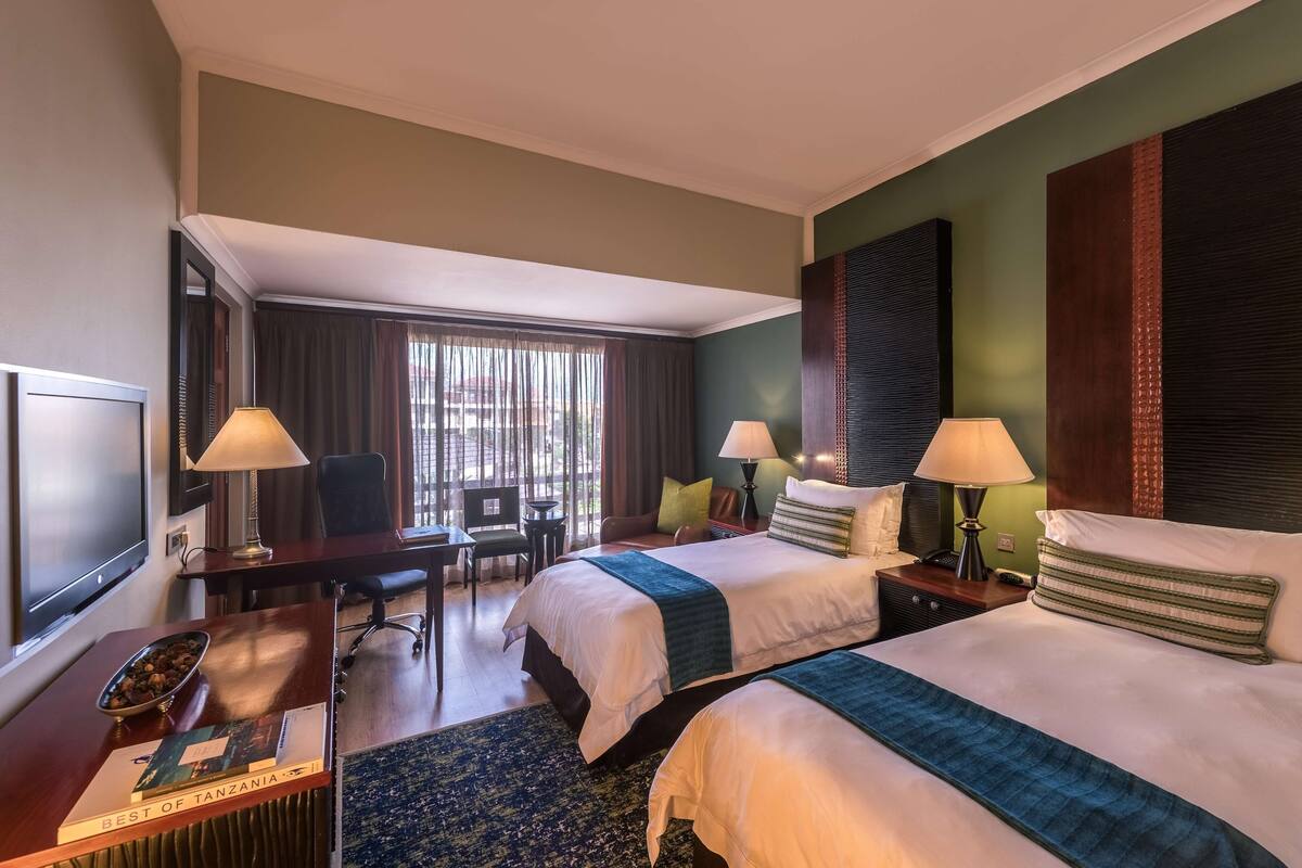 Une chambre d’hôtel avec deux lits, un bureau, une télévision et une fenêtre avec des rideaux.