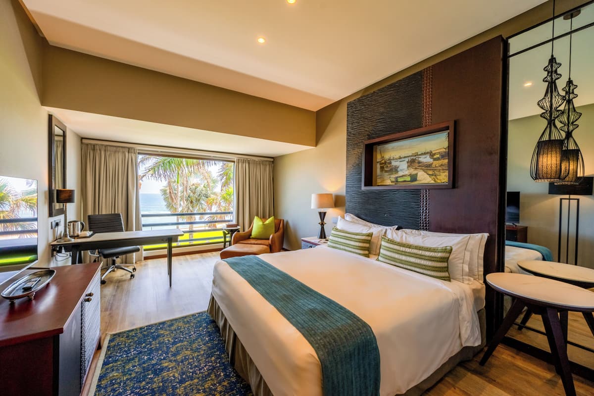 Une chambre d’hôtel avec un grand lit, un bureau, une chaise, une petite table et une vue sur l’extérieur.