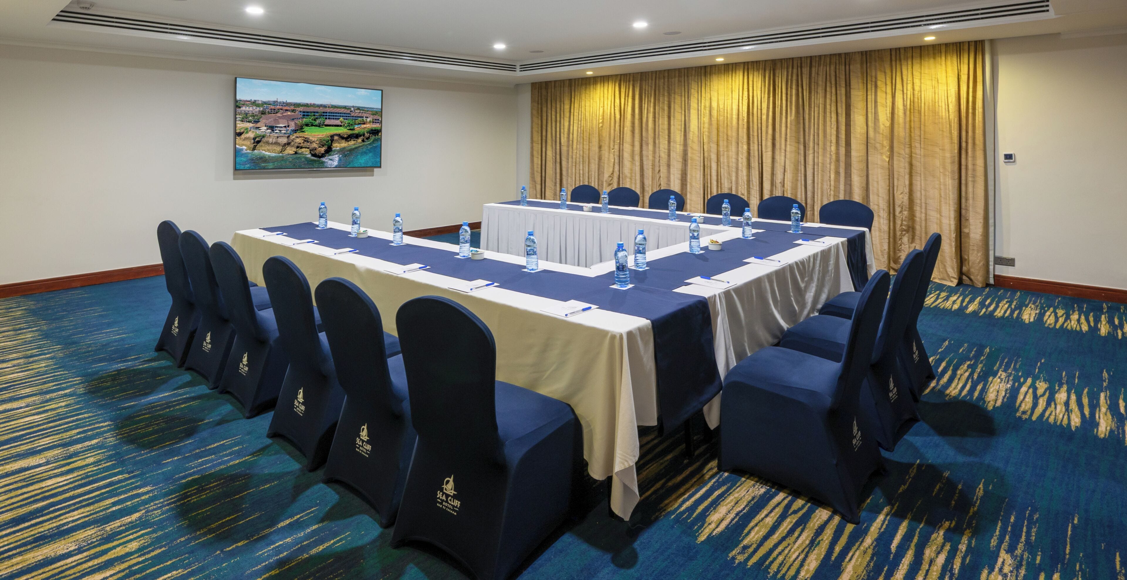 A conference room with a long table, chairs, water bottles, and a view of a coastal landscape.