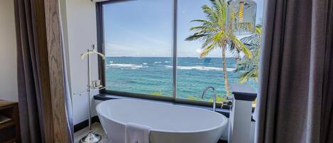 A modern bathroom with a freestanding bathtub, a large window offering a view of the ocean, and a hanging light fixture.
