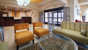 A lobby with a reception desk, seating area with patterned chairs and sofas, a glass coffee table, and a stone fireplace. - Best Western Plus Desoto Inn & Suites (Mansfield)