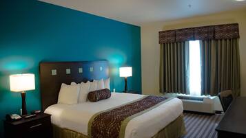 A hotel room with a large bed, two bedside lamps, a desk, and a window with curtains.