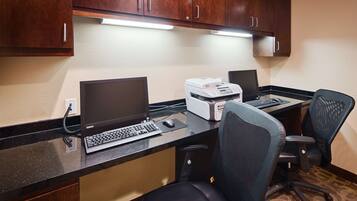 Um balcão de hotel com um computador de mesa, impressora e duas cadeiras de escritório.