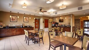 A hotel dining area with a bar, multiple tables and chairs, ceiling fans, and wall-mounted artwork. - Best Western Plus Desoto Inn & Suites (Mansfield)